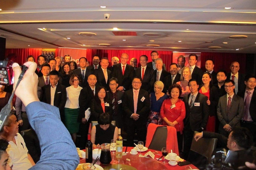 A large group of people pose for a photo in front of red curtains.