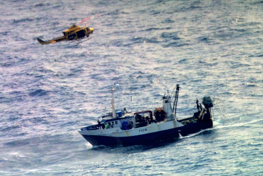 A helicopter hovering above a fishing trawler in the ocean.