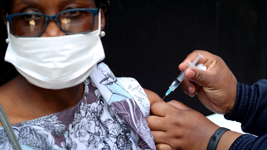 A woman wearing glasses and a white mask receives the vaccination