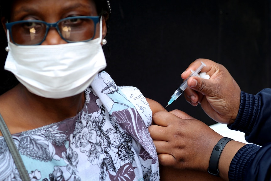 Woman wearing glasses and white mask receives vaccination