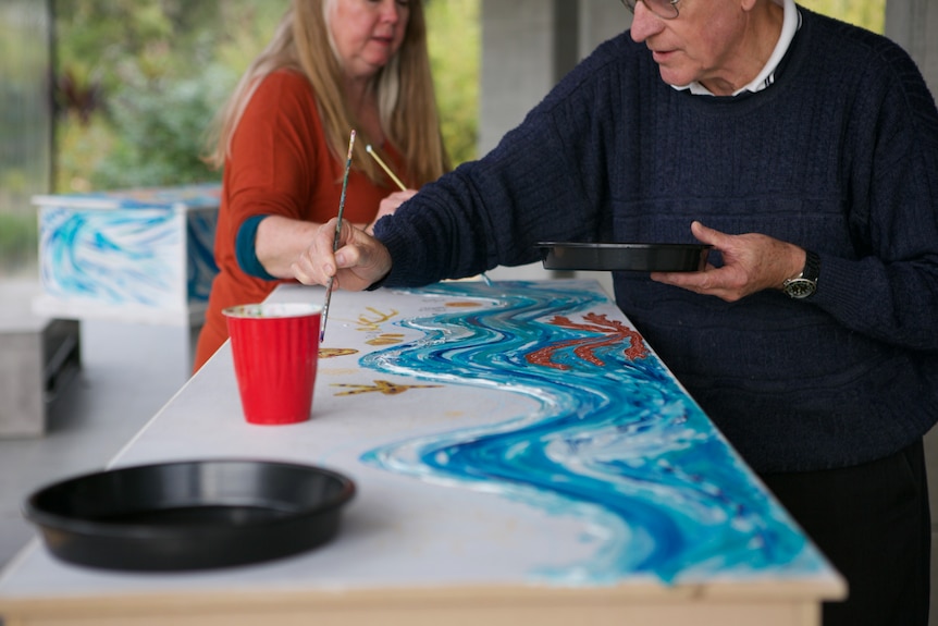 Two people painting a coffin. 