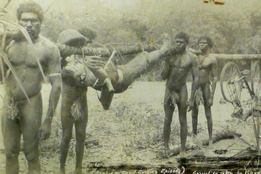Tribesmen carrying Ryko on a log.