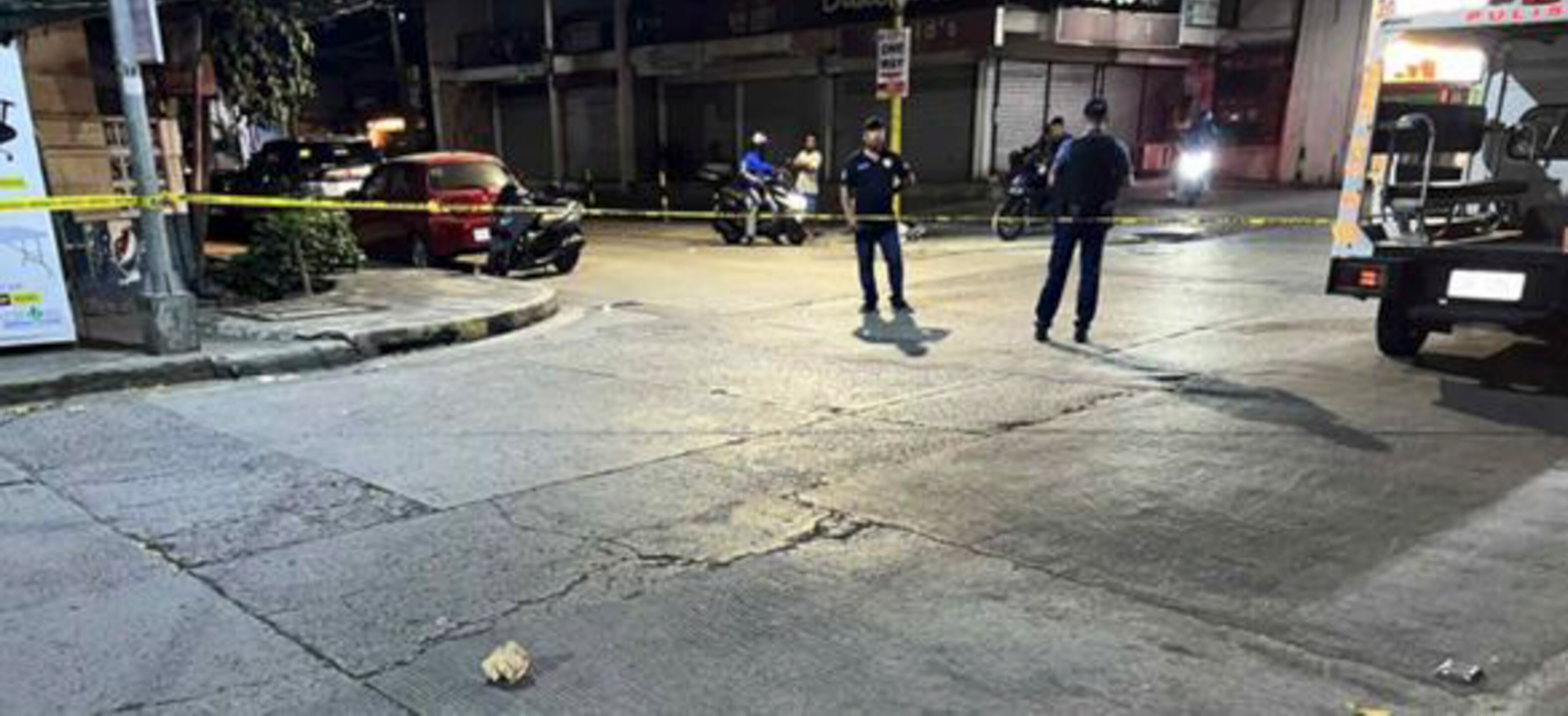 Two police officers stand at cordoned off street at night.