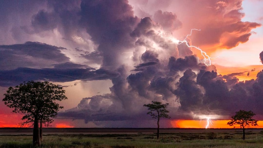 A thunderstorm rolls across a red sky in the country.