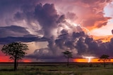 A thunderstorm rolls across a red sky in the country.