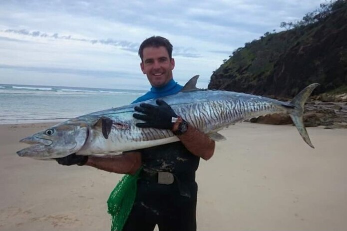 A man smiling while holding a large fish on a beach