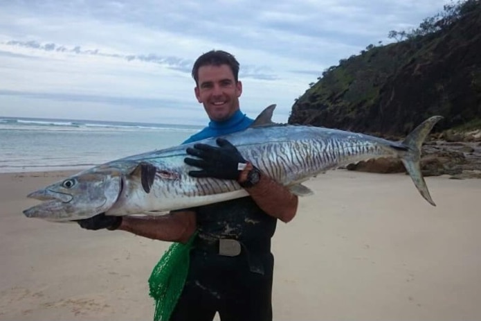 A man smiling while holding a large fish on a beach