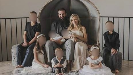 Two parents and seven children sit while posing for a family photo