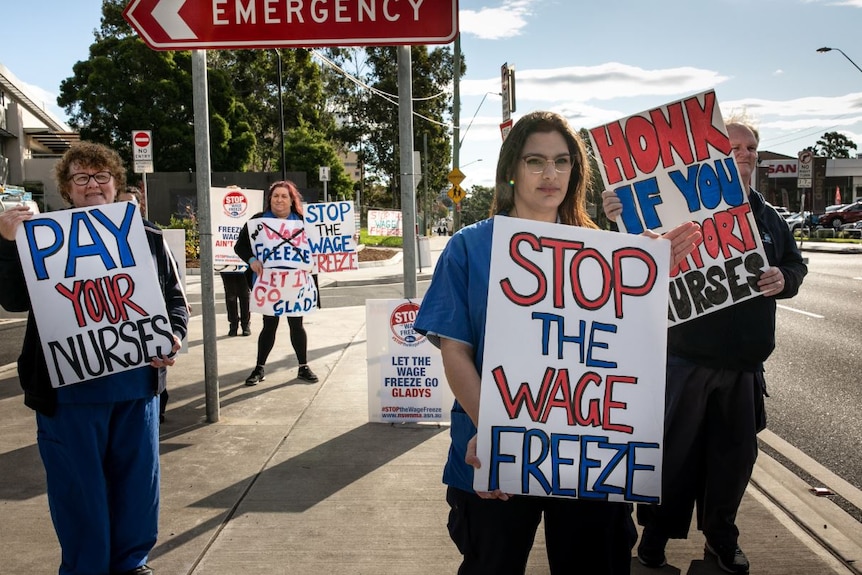 Nurses hold posters on the side of a road which read 'Stop the wage freeze'