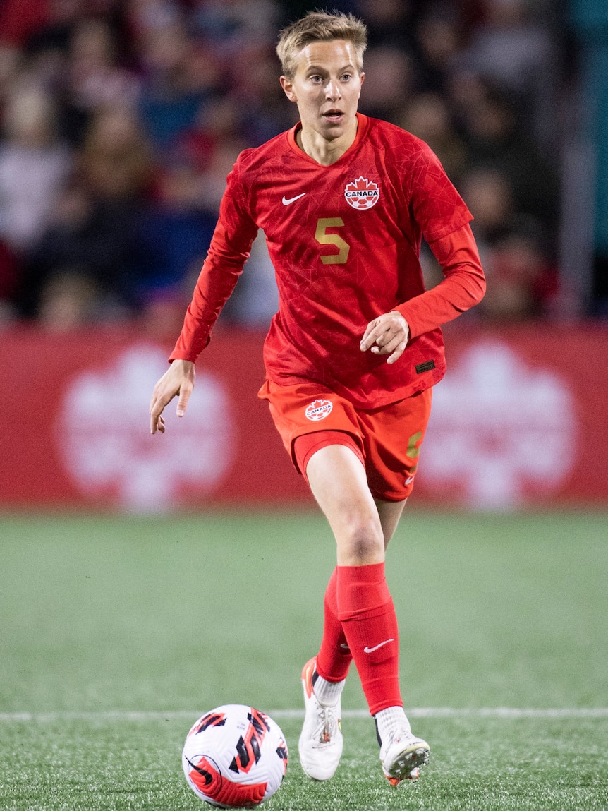 A soccer player wearing all red runs with the ball on the pitch during a match