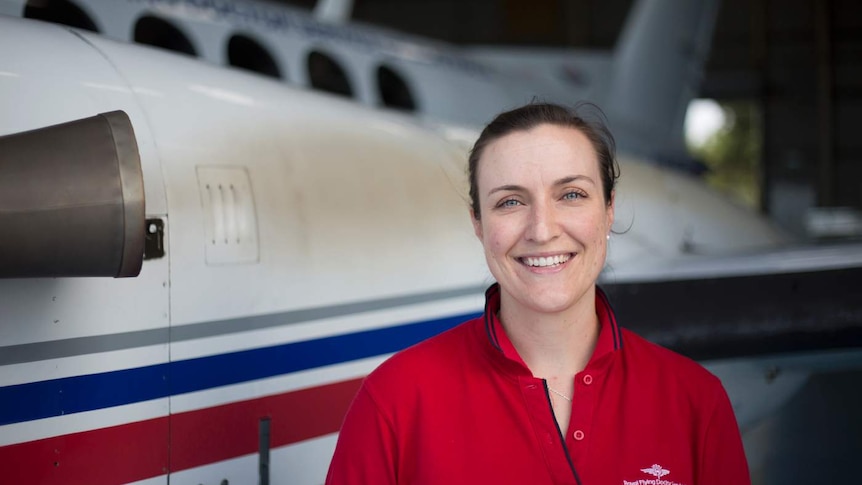 A woman stands in front a of an RFDS plane in the hanger