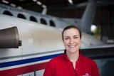 A woman stands in front a of an RFDS plane in the hanger