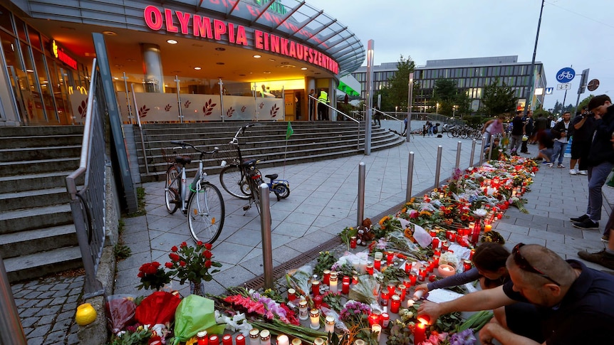 People lay flowers in front of Olympia shopping mall