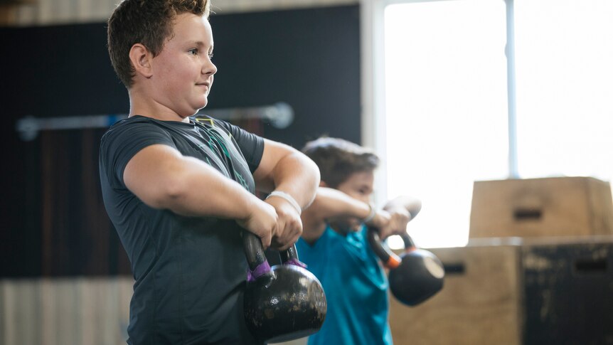 A young boy is lifting a kettlebell in front of his chest