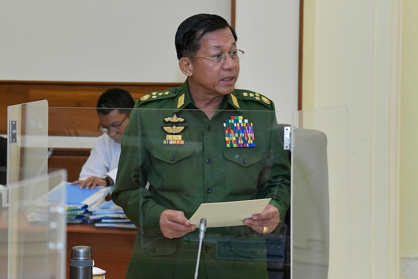 A military general in uniform holds paper as he talks to a defence council. 