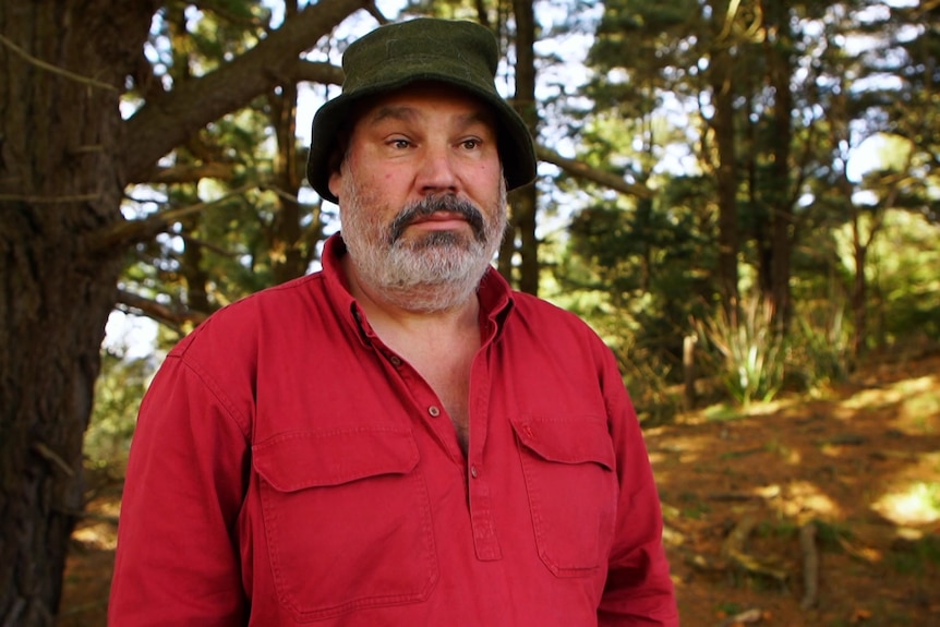 Man in red shirt and bucket hat standing in a forest.