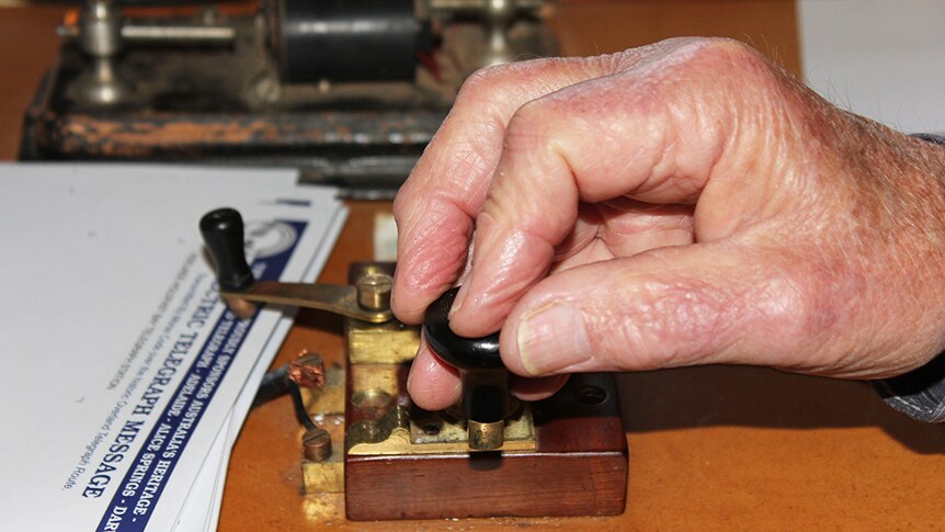 A close-up of a hand using a Morse code machine to send a telegram.