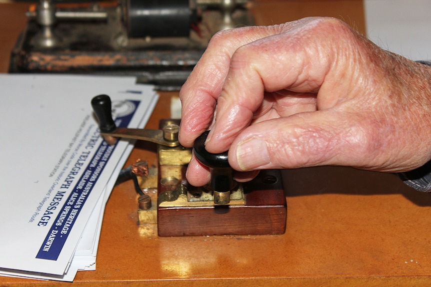 A close-up of a hand using a Morse code machine to send telegrams.