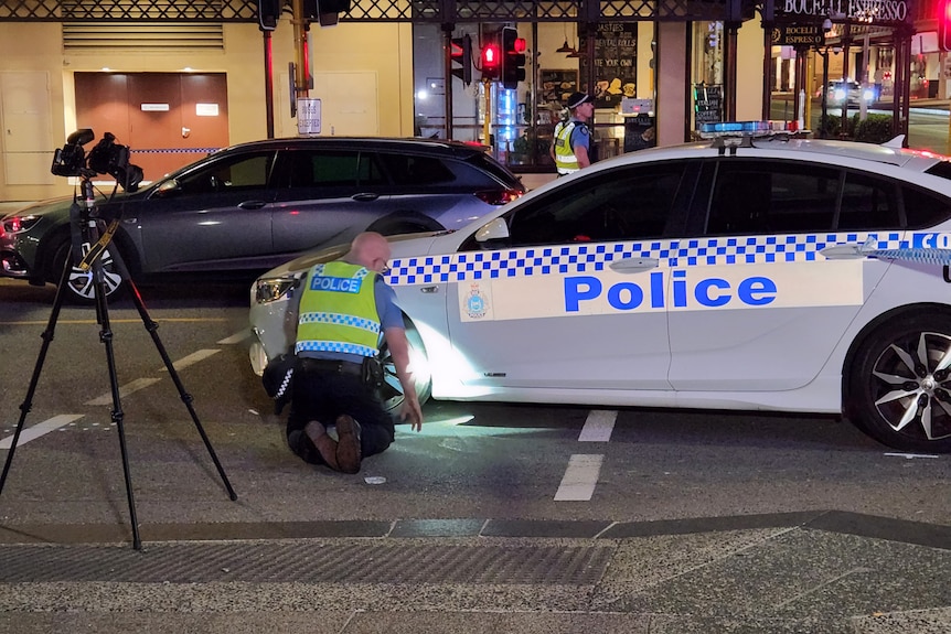 A police officer shines a torch on a police car on a street