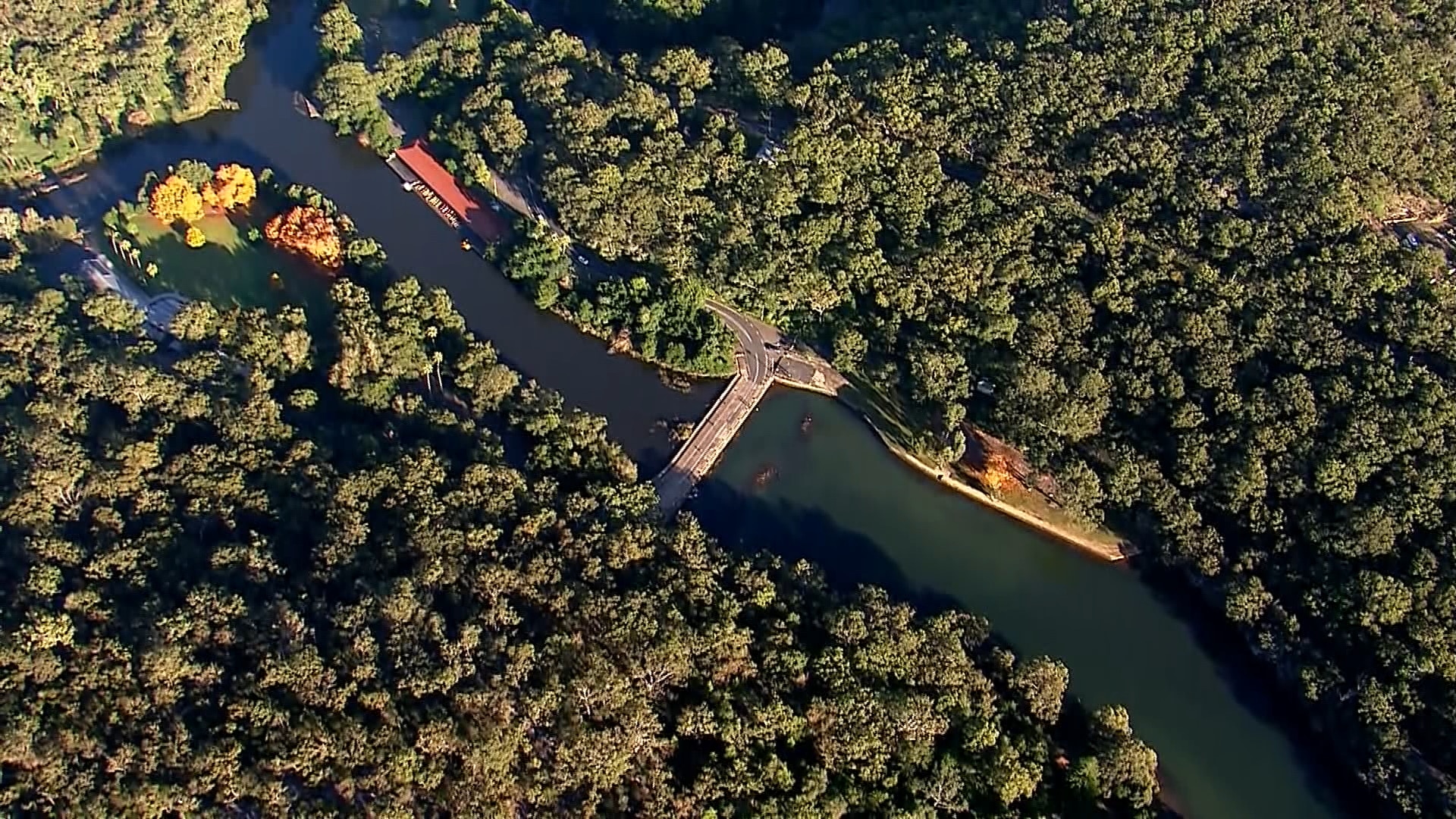 A wide aerial shot of a body of water winding around land with trees and a road crossing connecting both sides.