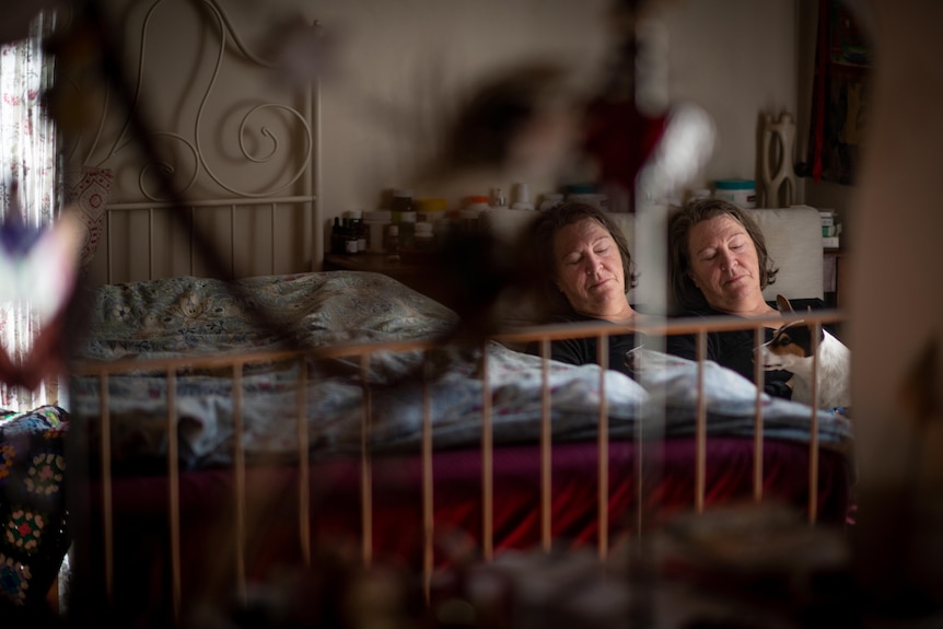 A middle-aged white woman lying in bed looking exhausted. She is reflected in a small mirror