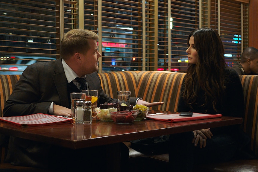 Colour photograph of James Corden and Sandra Bullocksitting at a diner booth at night time in 2018 film Ocean's 8.