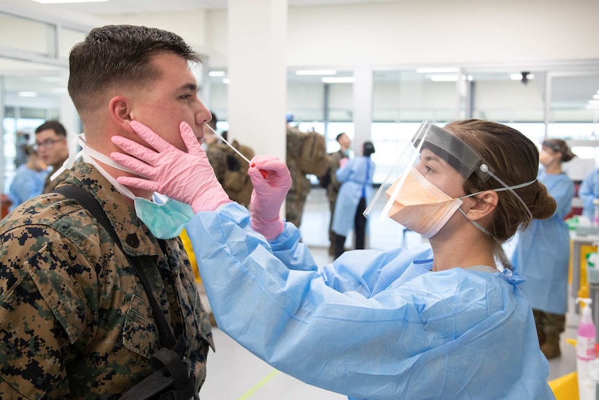 A US Marine is screened for coronavirus as a nurse takes a nose swab.
