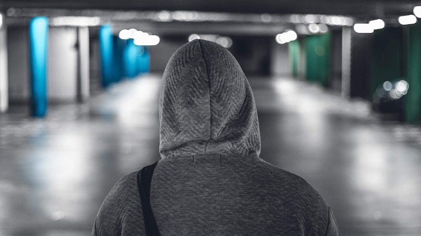 A person in a hooded jumper stands facing away in a parking lot.