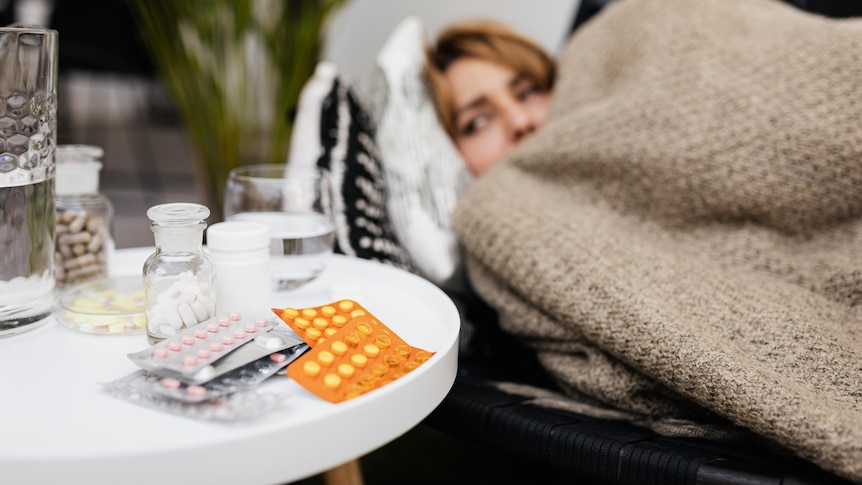 A woman lying in bed with medications next to her