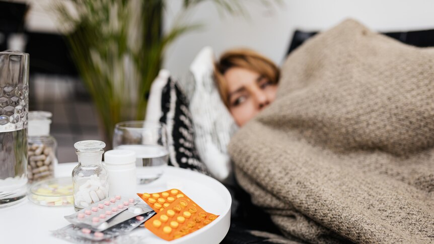 A woman lying in bed with medications next to her