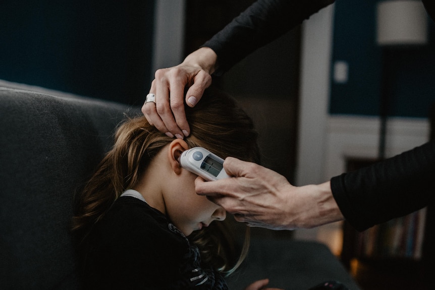 Mother takes the temperature of her daughter with an ear thermometer.