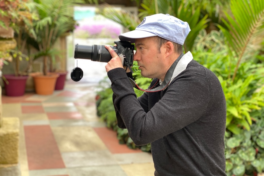 A man looks through a camera viewfinder in a hot house