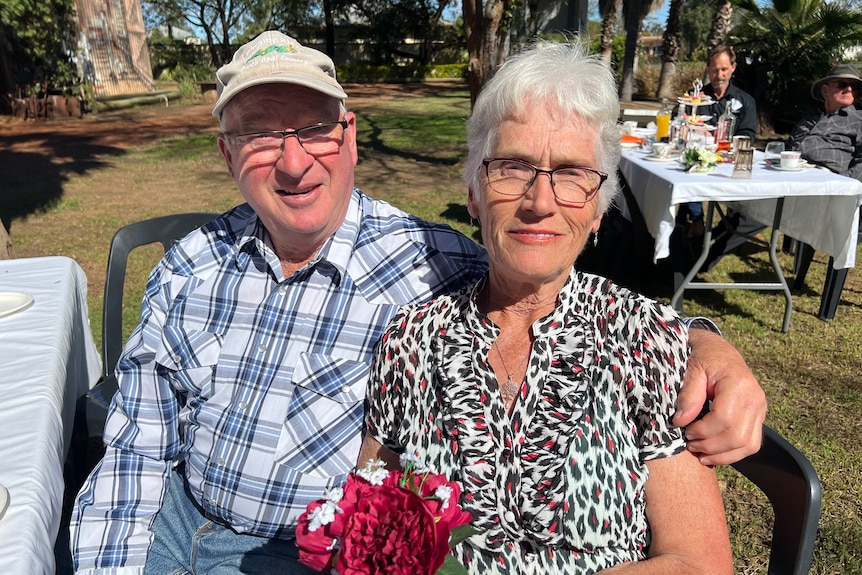 An elderly couple sits outside with a bourquet of flowers