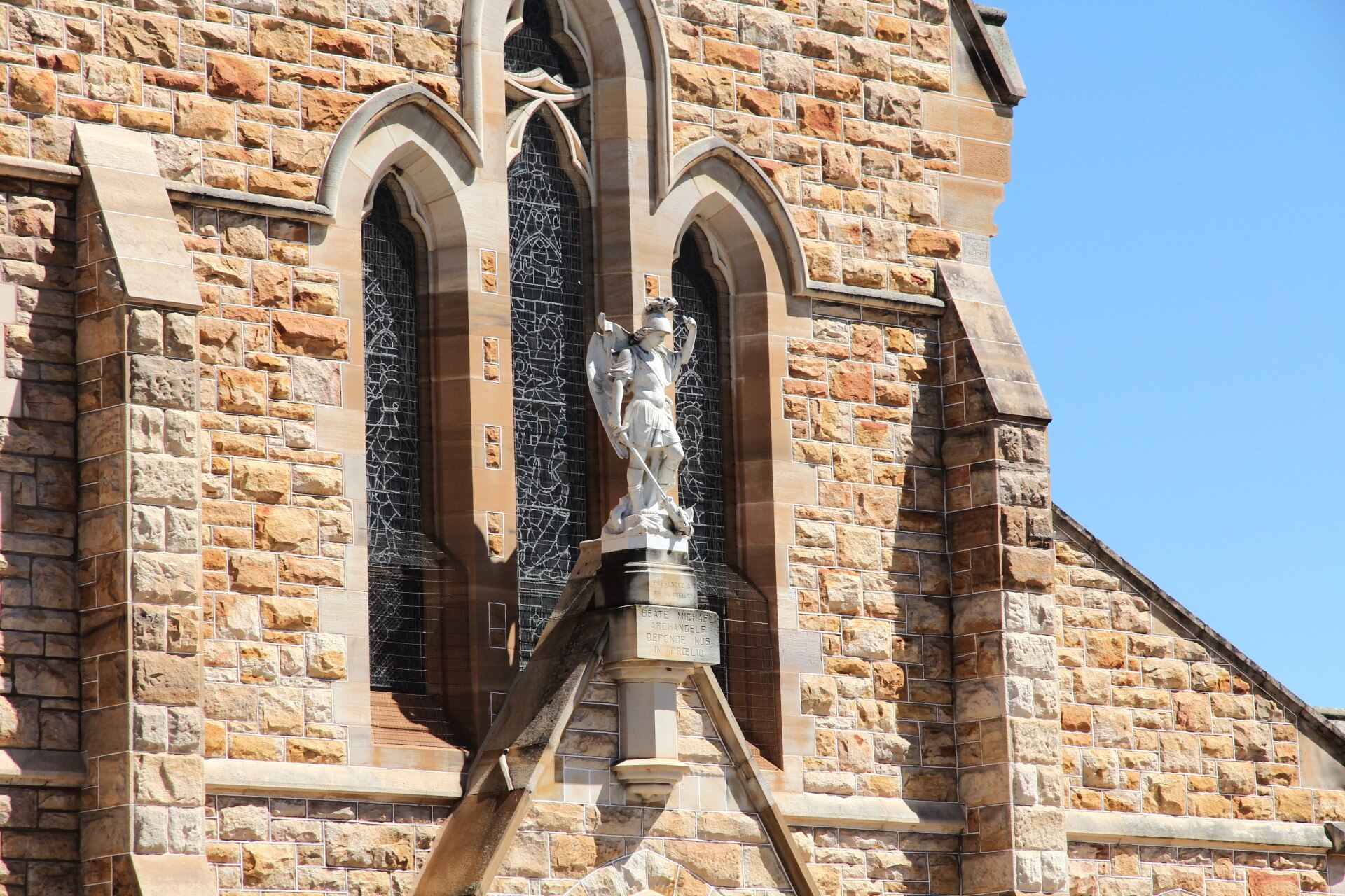 A white statue in the centre of the picture, surrounded by sandstone and stained glass windows behind