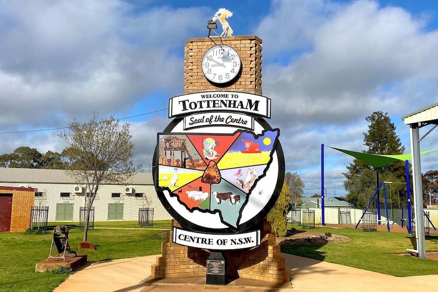 A large and colourful sign in the shape of NSW is connected to a vertical brick structure with a clock at the top.