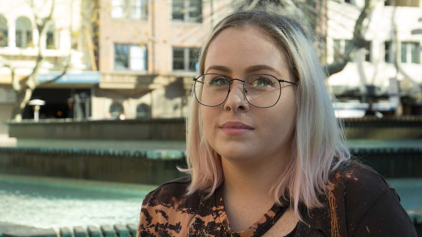 A young woman stands next to a fountain in a public space in Sydney.