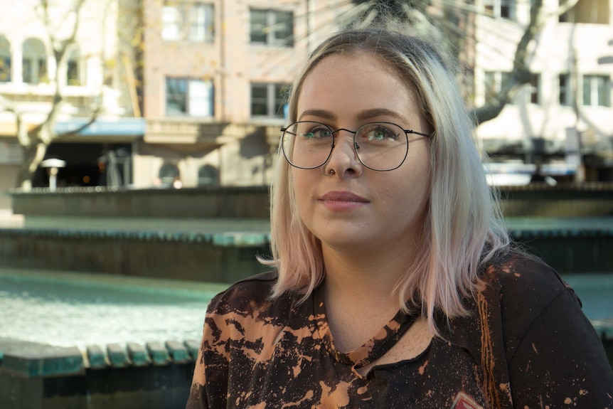 A young woman stands next to a fountain in a public space in Sydney.