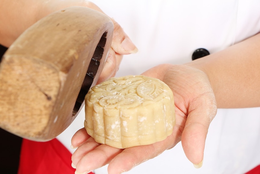 Person holding an unbaked moon cake and a wooden moulding paddle.