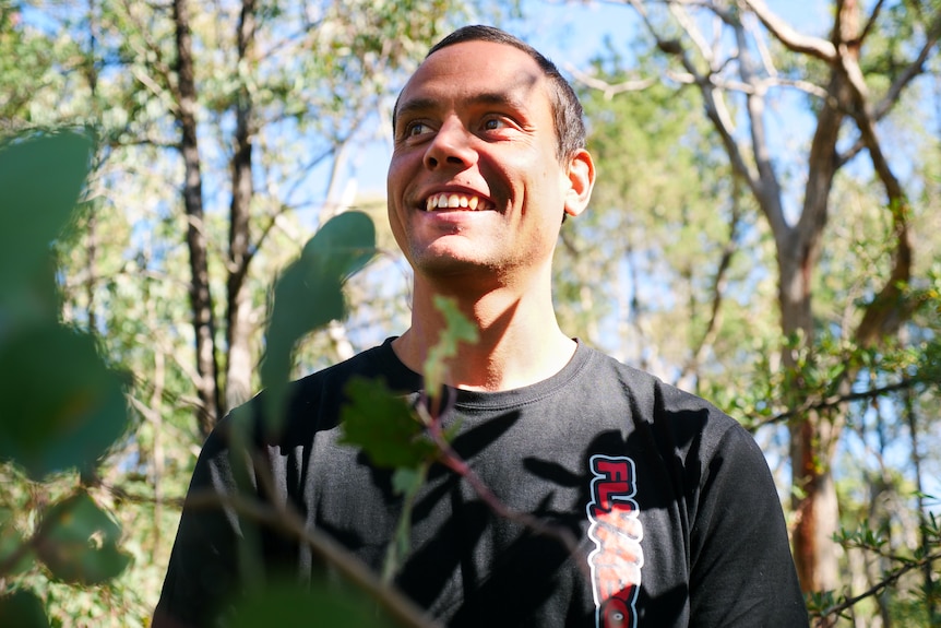 A young Indigenous man looks away from the camera smiling.