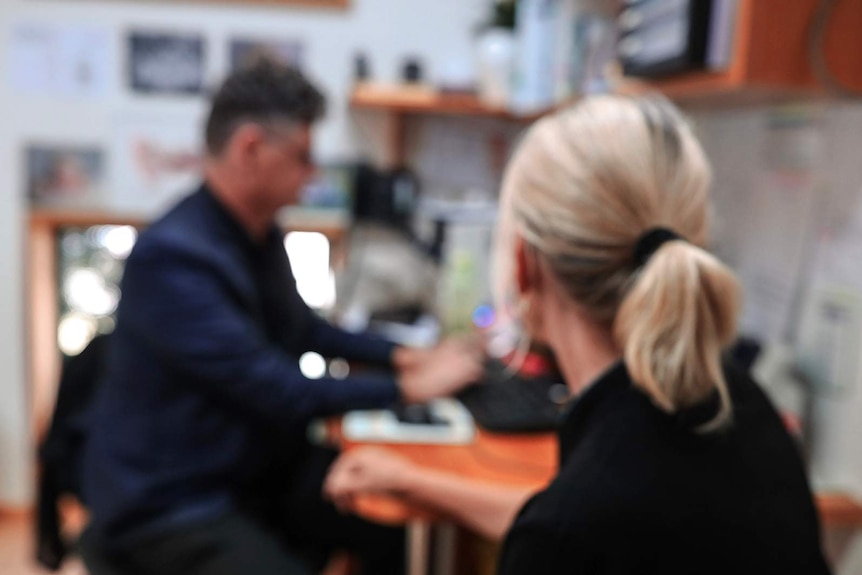 A generic photo of a male doctor and patient consultation in a GP's practice. Doctor is blurred, patient, has back to camera.