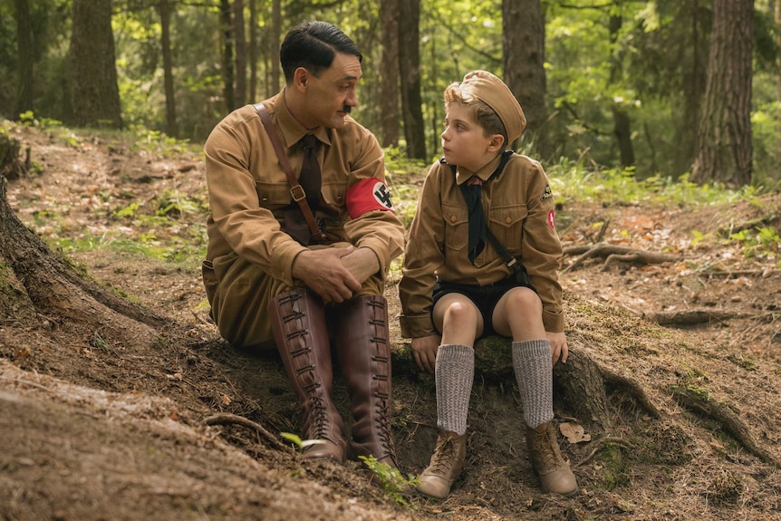 A young boy sits in a forest with an actor playing Hitler.