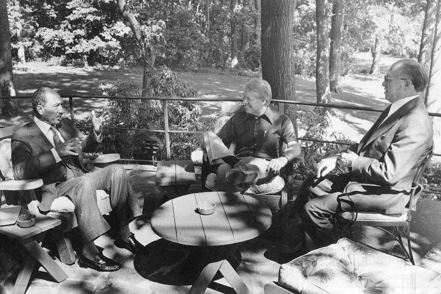 Anwar El Sadat, Jimmy Carter and Menachem Begin sit around an outdoor table at Camp David.