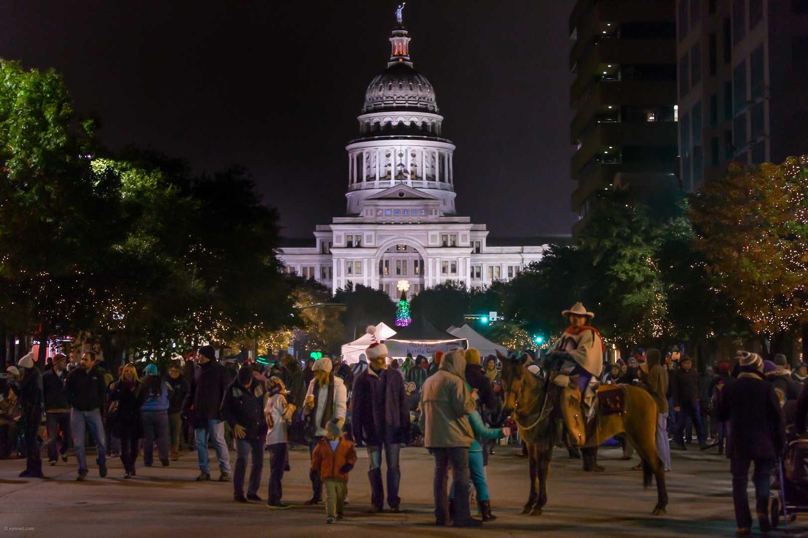 A large crowd in winter clothes, including a man on a horse, in front of the Texas State Capitol building.