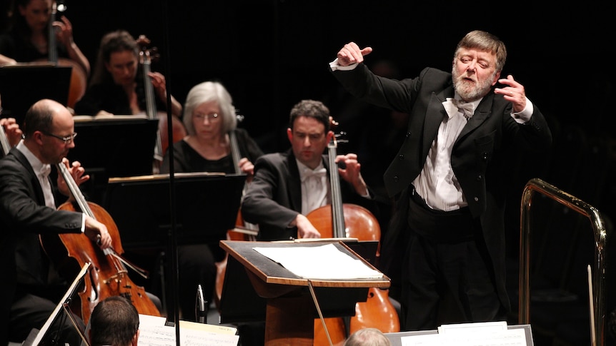 A man wearing tails and a white bow tie conducts an orchestra.