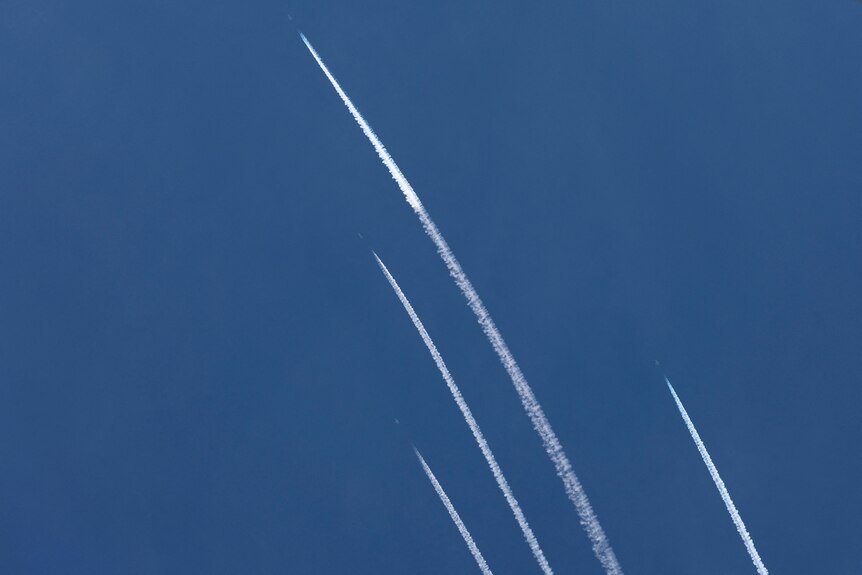 Four white lines trace the blue sky as rockets are fired.