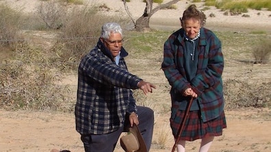 A man and a woman in the desert pointing at a site.