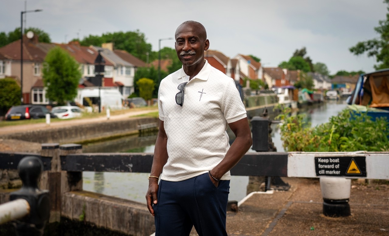 A man standing near a canal, smiling at the camera.