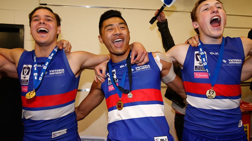 Three AFL players in red, white and blue raucously sing, with arms around each other