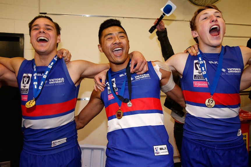 Three AFL players in red, white and blue raucously sing, with arms around each other