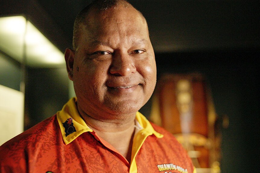A middle-aged man in a red and yellow polo shirt smiles at the camera.